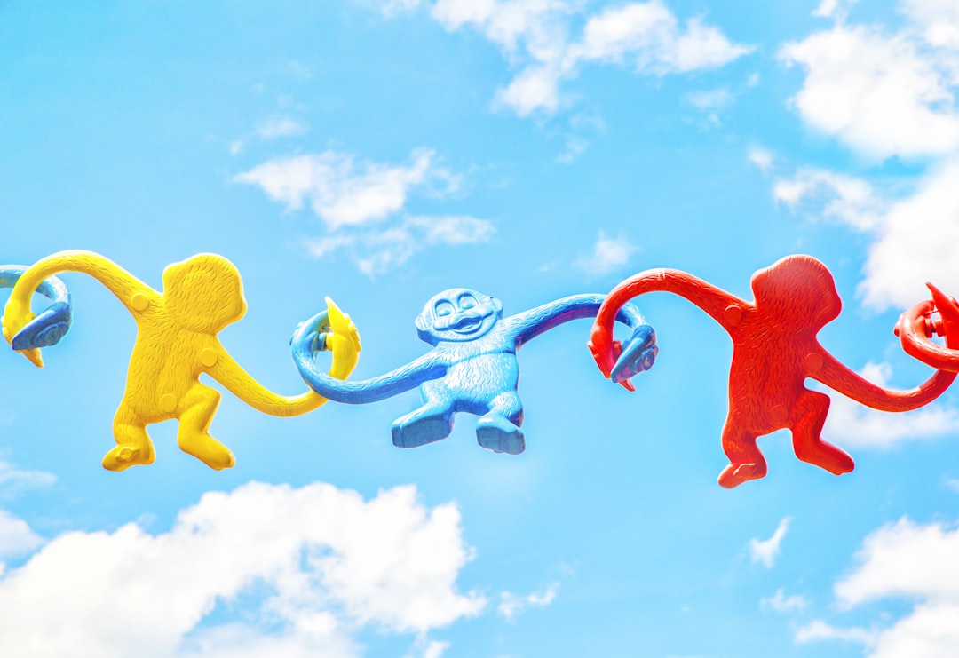 three assorted-color monkey plastic toys holding each other during daytime playful logos mascot cartoon pastel